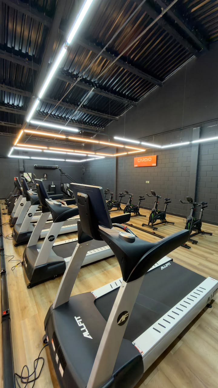Área de cardio com esteiras ALLFIT, bikes e escada ergométrica sob iluminação em LED